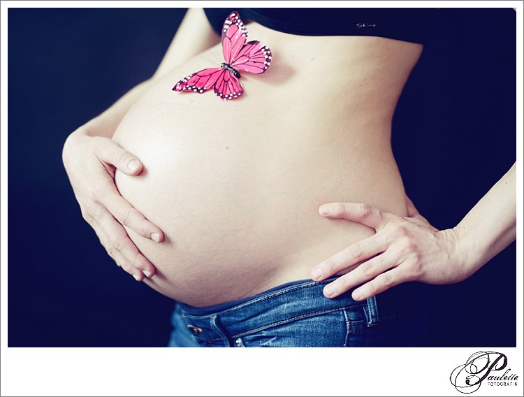 Nahaufnahme eines Babybauch im 9. Monat mit rosa Schmetterling. 